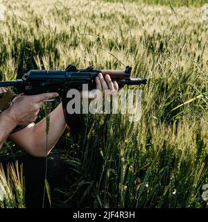 Un soldato con fucili d'assalto militari da combattimento AK 74 si trova in un campo, campi di grano ucraini e guerra, movimento di guerriglia in ucraina, guerriglia venduto Foto Stock