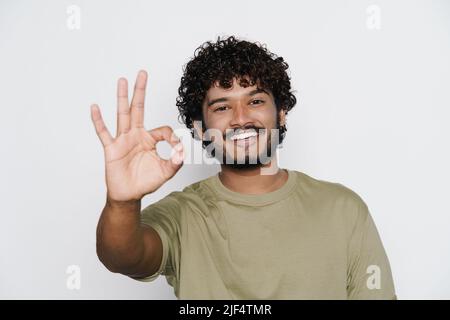 Giovane uomo bearded sorridendo mentre mostra il gesto di ok isolato su sfondo bianco Foto Stock