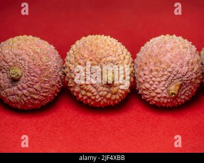 Lychee sul tavolo. Prugna cinese su sfondo rosso. Frutta matura dall'Asia. Prodotto delizioso e succoso. Foto Stock