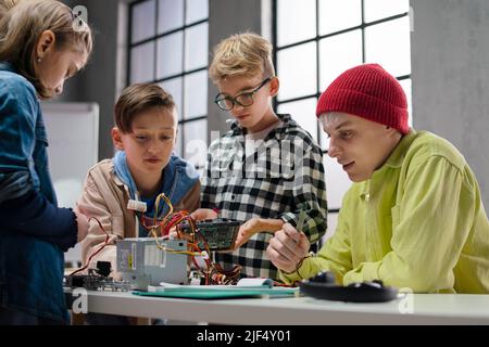 Ragazzi con insegnante che lavorano insieme al progetto con giocattoli elettrici e robot in classe robotica Foto Stock