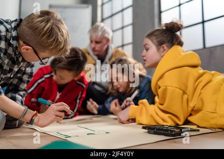 Ragazzi con insegnante che lavorano insieme al progetto con giocattoli elettrici e robot in classe robotica Foto Stock