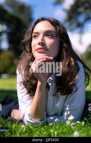 Ritratto di giovane donna che posa prono su erba in un parco Foto Stock