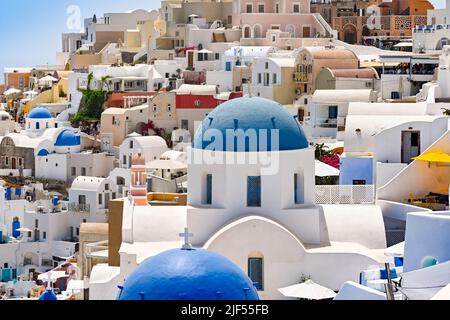 Oia, Santorini, Grecia - Giugno 2022: Edifici bianchi con cupole blu e altri edifici sul versante ripido della città di Oia. Foto Stock