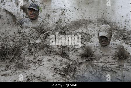 La gente gioca in acqua di fango in un campo di risaie durante la festa nazionale della risaia. Gli agricoltori nepalesi festeggiano il National Paddy Day con vari eventi che segnano l'inizio della stagione annuale di semina del riso. Foto Stock