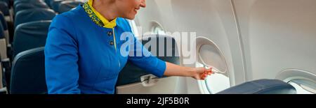 Donna sorridente stewardess chiusura finestra in aereo Foto Stock