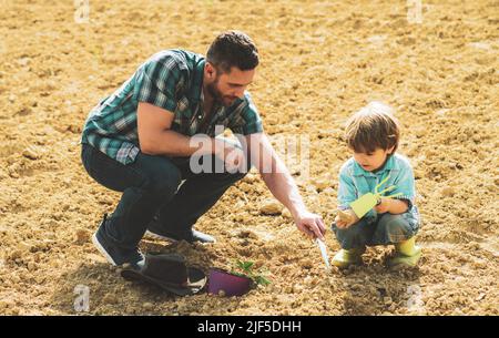 Padre e figlio che piantano. Piante crescenti. Giardino di primavera. Papà che insegna le piante di cura del figlio piccolo. Scavo e pala, Foto Stock
