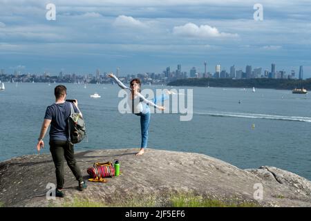 Una ballerina che si posa di fronte allo skyline e la sua amica che scatta una foto a Watsons Bay, Sydney, Australia Foto Stock