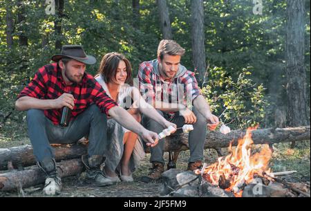 Gli amici possono godersi il barbecue nel fine settimana nella foresta. Amici della compagnia picnic o barbecue marshmallows tostatura vicino falò. Gruppo di backpackers rilassante vicino Foto Stock