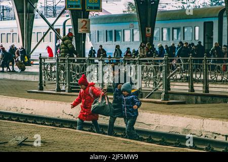 Madre sta attraversando la piattaforma con i suoi due figli. La stazione ferroviaria di Lviv è diventata uno dei punti focali più essenziali per i rifugiati che fuggono dalla guerra da est. Foto Stock