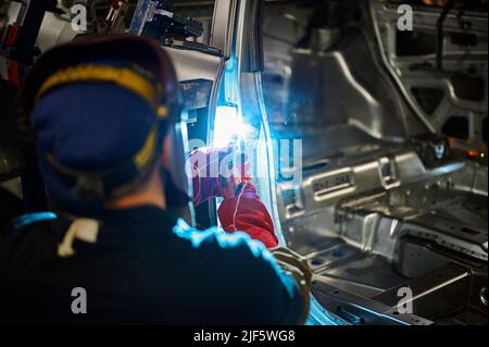 Il saldatore in casco lavora con parti metalliche della carcassa dell'automobile Foto Stock