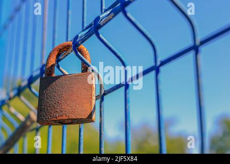 Un vecchio lucchetto arrugginito appeso su una griglia blu in Polonia Foto Stock