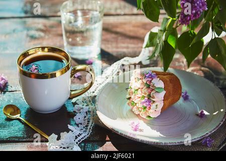 Ramo estivo all'aperto con una tazza di caffè, un bel cupcake, un bicchiere d'acqua e fiori luminosi. Cottage nucleo pic-nic con tonalità luminose estate di fiori in una giornata di sole. Ombre dure. Foto Stock