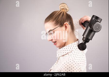 Donna sorridente con bretelle usa una pistola massaggiatore per la schiena. Foto Stock