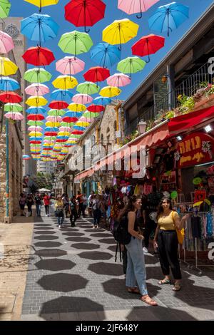 I pedoni camminano sotto ombrelli colorati sospesi sopra la via Yoel Solomon a Nahalat Shiva, il terzo quartiere costruito fuori dalla città Vecchia di Gerusalemme negli anni '1860 Oggi è un affollato viale pedonale fiancheggiato da caffetterie sul marciapiede. Gerusalemme Ovest Israele Foto Stock