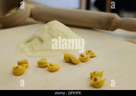 Tortellini crudi appena fatti su tavola di legno e un matterello e farina sullo sfondo. Foto Stock