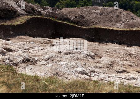 Fondo roccioso di un pozzo archeologico scavato su una collina alla ricerca di manufatti storici. Opere archeologiche Foto Stock