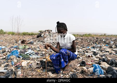 Ragazza africana seduta in mezzo a cumuli di rifiuti, incaricato di trovare materiali riciclabili come metallo, vetro e plastica; rifiuti informali ricicla Foto Stock
