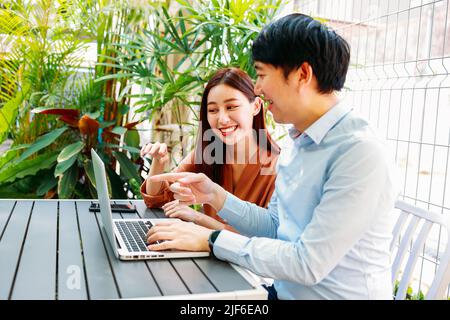 Felice asiatico giovane uomo allegro e donna seduto in moderno caffè mentre si lavora insieme e brainstorming sul piano di startup sul portatile Foto Stock