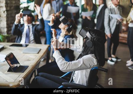 Diverse persone d'affari che indossano occhiali di realtà virtuale all'interno dell'ufficio - Focus su ragazza africana seduta su sedia a rotelle Foto Stock