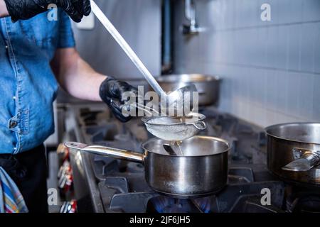 Lo chef separa l'acqua dal riso utilizzando il filtro nella cucina commerciale Foto Stock