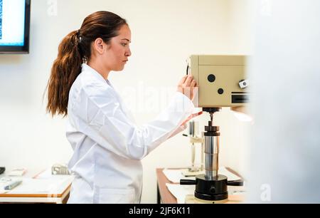 Vista laterale di una scienziata femminile seria in accappatoio medico messa a punto attrezzature moderne per la ricerca mentre si lavora in laboratorio leggero Foto Stock