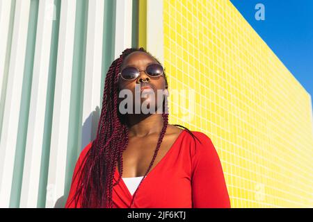 Donna afroamericana incinta positiva con capelli ricci che sorridono felicemente mentre tocca il pancino e guarda la macchina fotografica Foto Stock