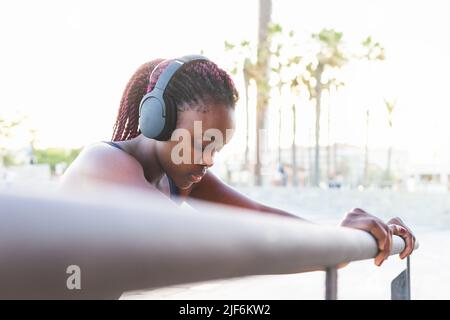 Vista laterale dell'atleta femminile in FIT in abbigliamento sportivo e cuffie che si allungano durante il riscaldamento prima dell'allenamento Foto Stock