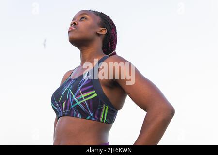 Dal basso di FIT Black atleta donna in abbigliamento sportivo riposante dopo essersi allenato contro il cielo limpido Foto Stock