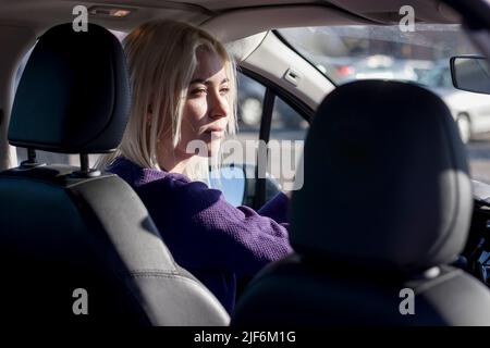 Bruna caucasica carina che guida la sua auto . Foto scattata dal sedile posteriore. Foto Stock