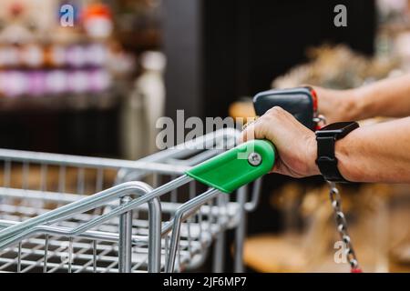 Donna anziana irriconoscibile con orologio intelligente che spinge carrello e camminare vicino scaffali in negozio di fiori Foto Stock