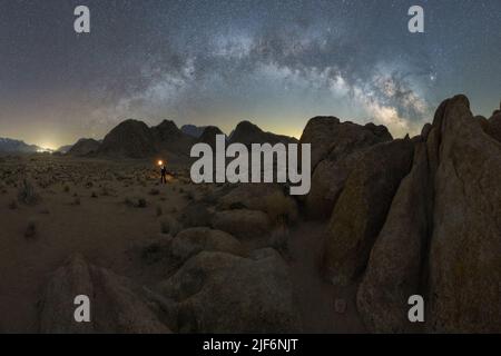 Silhouette di esploratore irriconoscibile in piedi con torcia sul paesaggio di formazioni rocciose negli altopiani sotto il cielo stellato via lattiginosa in Alabama Hills Foto Stock
