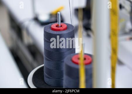 Bobine a fuoco morbido di fili scuri poste su macchine da cucire professionali in moderne officine leggere con attrezzature speciali durante il processo di cucitura Foto Stock