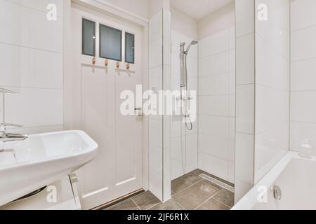 Lavandini con specchi e vasca pulita situati vicino a box doccia con porta in vetro in bagno moderno con pareti piastrellate bianche Foto Stock