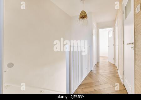 Corridoio stretto con molte porte in pareti bianche e lampada luminosa sul pavimento in legno Foto Stock