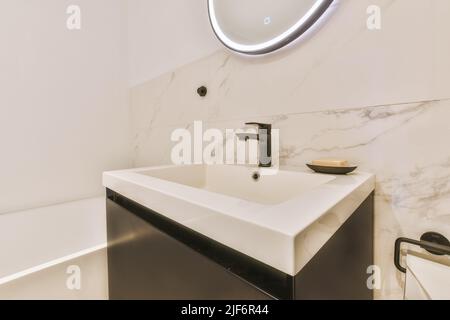 Lavandino con rubinetto e sapone liquido appeso su una parete piastrellata sotto lo specchio in bagno contemporaneo a casa Foto Stock