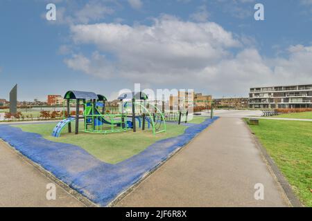 Moderno parco giochi all'aperto con scivoli situato nel quartiere residenziale della città con edifici contemporanei contro il cielo blu nuvoloso Foto Stock