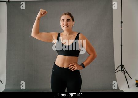 Giovane donna che flette i muscoli del braccio in uno studio Foto Stock