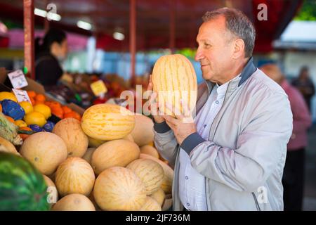 Uomo che sceglie i meloni nel negozio di frutta Foto Stock