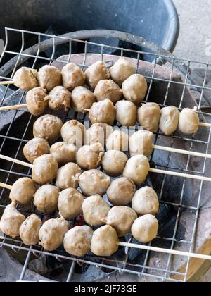 Le tradizionali polpette di maiale in stile thailandese con gli spiedini vengono grigliate su una griglia di metallo sulla stufa, vista frontale con lo spazio copia. Foto Stock