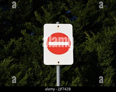 Un segno senza parole bianco e rosso di non ingresso, fissato ad un palo di metallo mediante bulloni arrugginiti, con un grande albero verde sullo sfondo Foto Stock