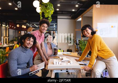 Ritratto di sorridenti architetti multirazziali maschili e femminili con modello architettonico in ufficio Foto Stock