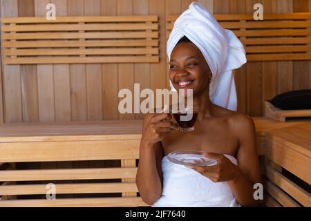 Allegra giovane donna afroamericana che guarda via mentre si beve sano in sauna, spazio copia Foto Stock