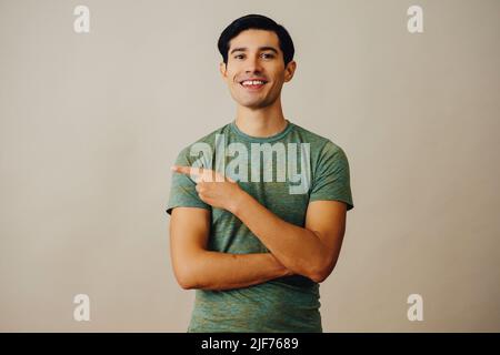 Ritratto l'uomo latino ispanico che punta verso il lato dello spazio di copia capelli neri sorridenti bella giovane adulta verde t-shirt su sfondo grigio guardando fotocamera studio scatto Foto Stock