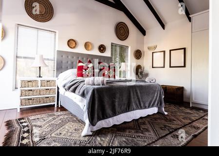 Letto con coperte e cuscini e decorazioni appese su pareti bianche in camera da letto moderna, spazio copia Foto Stock