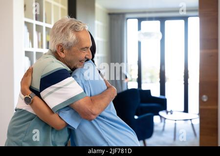 L'uomo anziano caucasico e l'operatore sanitario biraciale femminile si abbracciano a casa Foto Stock