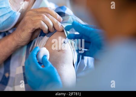 Professionista della salute femminile biracale che fa un'iniezione all'anziano caucasico a casa Foto Stock