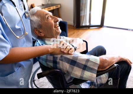 Parte centrale dell'operatore sanitario femminile che sostiene l'anziano caucasico seduto sulla sedia a rotelle Foto Stock