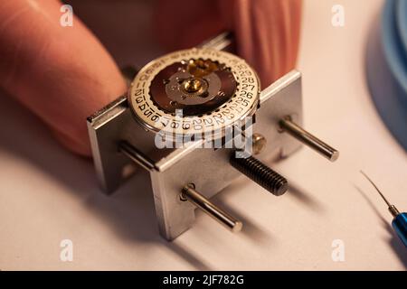 Guarda la riparazione presso il produttore di orologi. Concentratevi sul disco della data all'interno della custodia. Manutenzione di orologio. Immagine di primo piano con messa a fuoco selettiva. Foto Stock