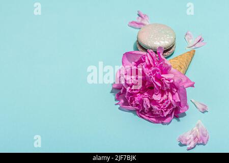 Coni di waffle al gelato con peonia e macaron su sfondo blu. Dolce dessert, petali di fiori, concetto estivo. Stile romantico, biglietto festivo, copia sp Foto Stock