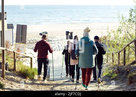 Vista posteriore dei campeggiatori di gruppo della gente con gli zaini che fanno nordic walking con i bastoni professionali che vanno giù alla spiaggia di mare Foto Stock